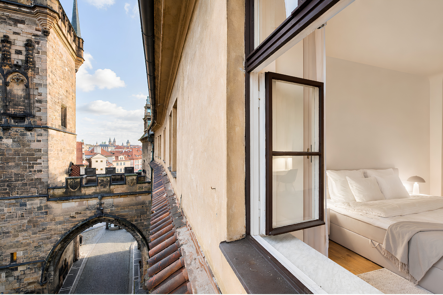 The bedroom window opening directly beside the Lesser Town Bridge Tower, with Old Prague beyond